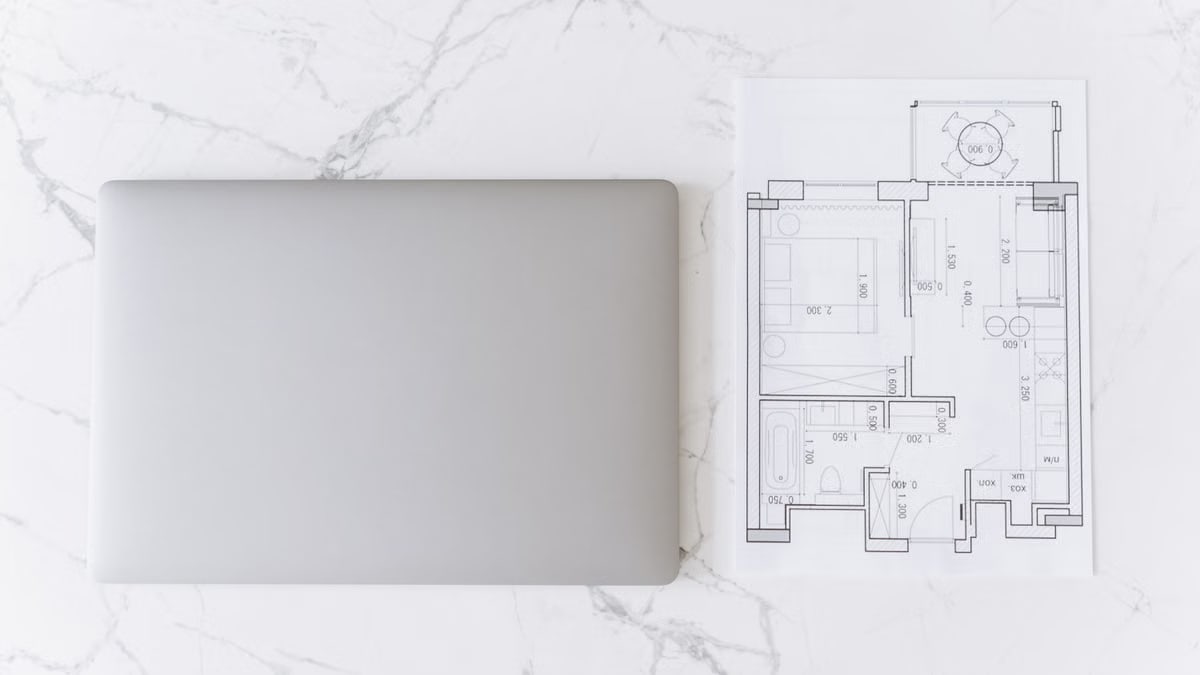 Top view of a laptop and architectural blueprint on white marble surface, showcasing modern workspace.